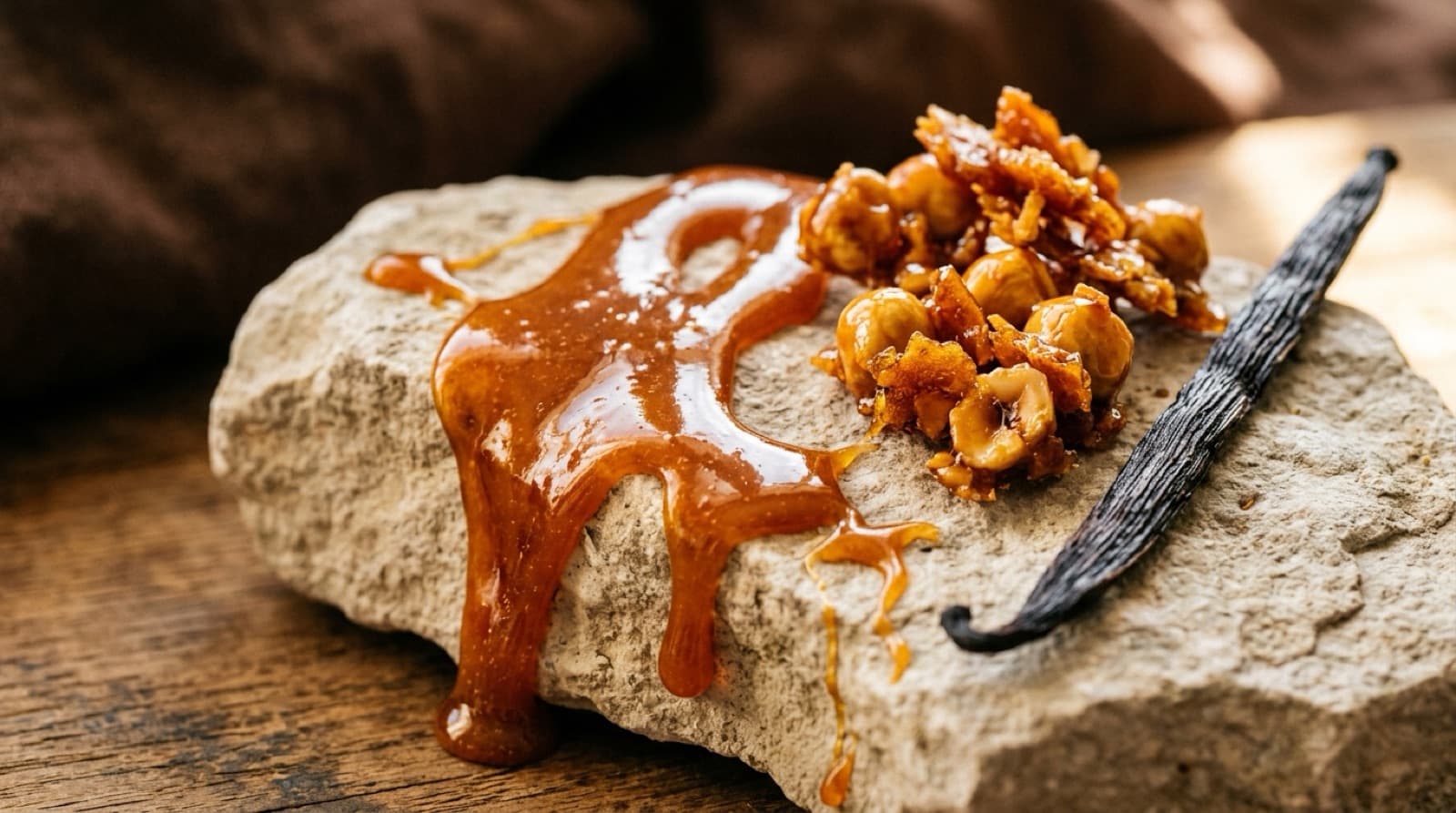 Caramel ambré coulant, éclats de praline et gousse de vanille sur une pierre claire.