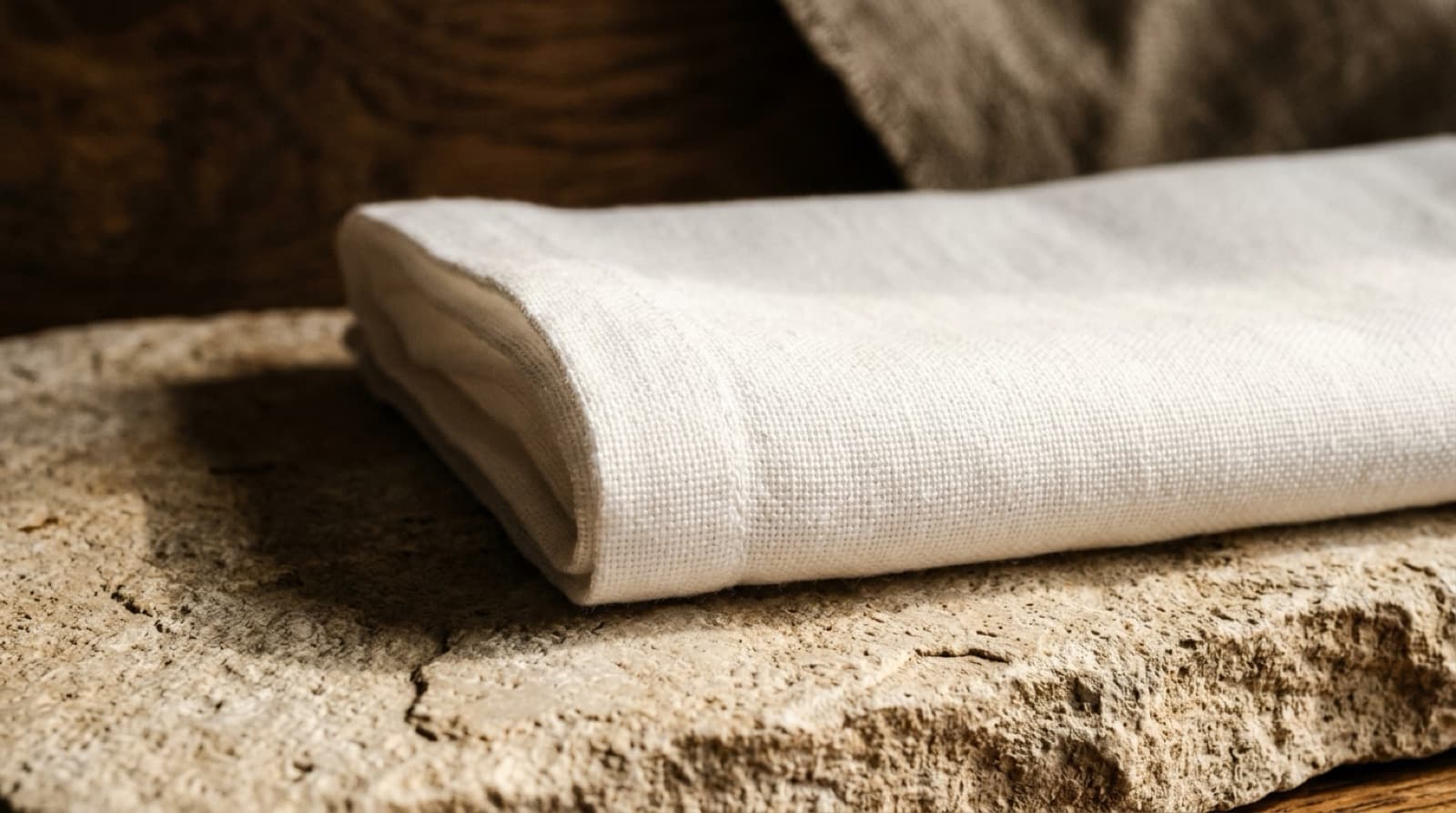 Linge de coton blanc plié sur une pierre claire, à la lumière rasante.