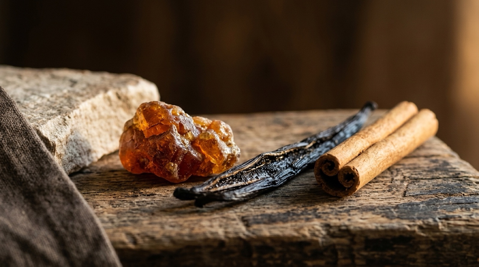 Résine de benjoin ambrée, gousse de vanille et bâton de cannelle disposés sur du bois patiné.