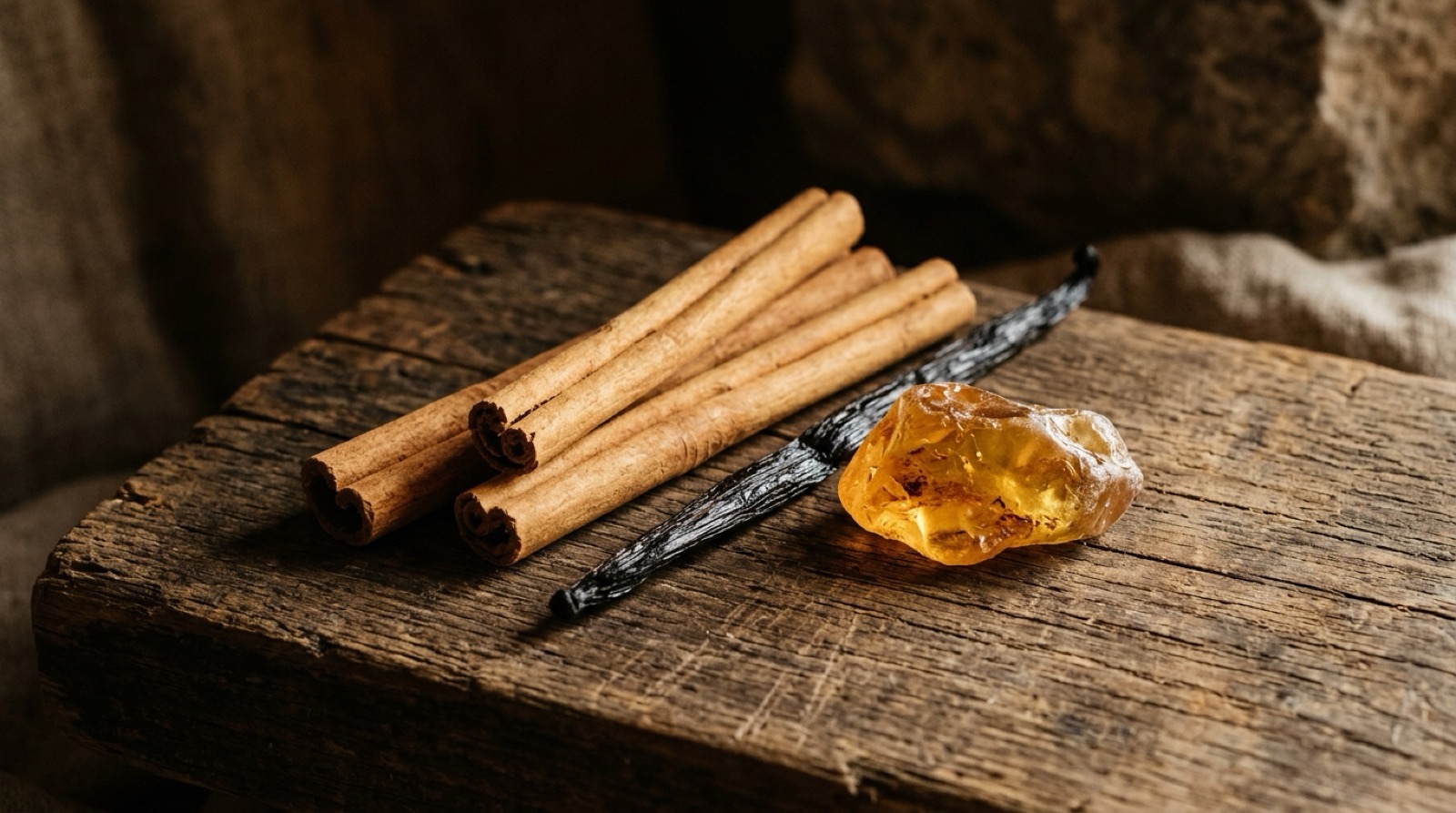 Bâtons de cannelle, gousse de vanille et morceau de résine ambrée sur du bois patiné.